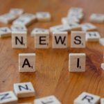 Peças de madeira formam as palavras “AI” e “NEWS” sobre uma superfície clara.
