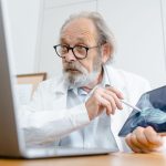 Médico de jaleco explica uma imagem de raio X usando um tablet em um consultório.