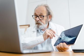 Médico de jaleco explica uma imagem de raio X usando um tablet em um consultório.