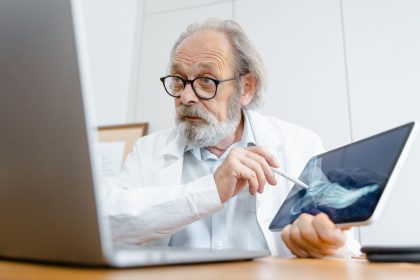Médico de jaleco explica uma imagem de raio X usando um tablet em um consultório.