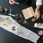 Vista superior de uma pessoa preparando perfume artesanal com ingredientes naturais sobre uma mesa de trabalho