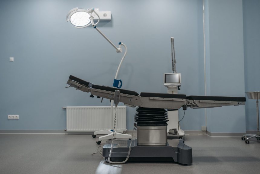 Sala de cirurgia moderna, vazia, equipada com mesa cirúrgica e aparelhos médicos.