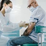 Profissional de saúde aplica uma vacina em uma pessoa idosa em ambiente clínico.