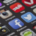Smartphone exibindo ícones de aplicativos de redes sociais sobre fundo claro.